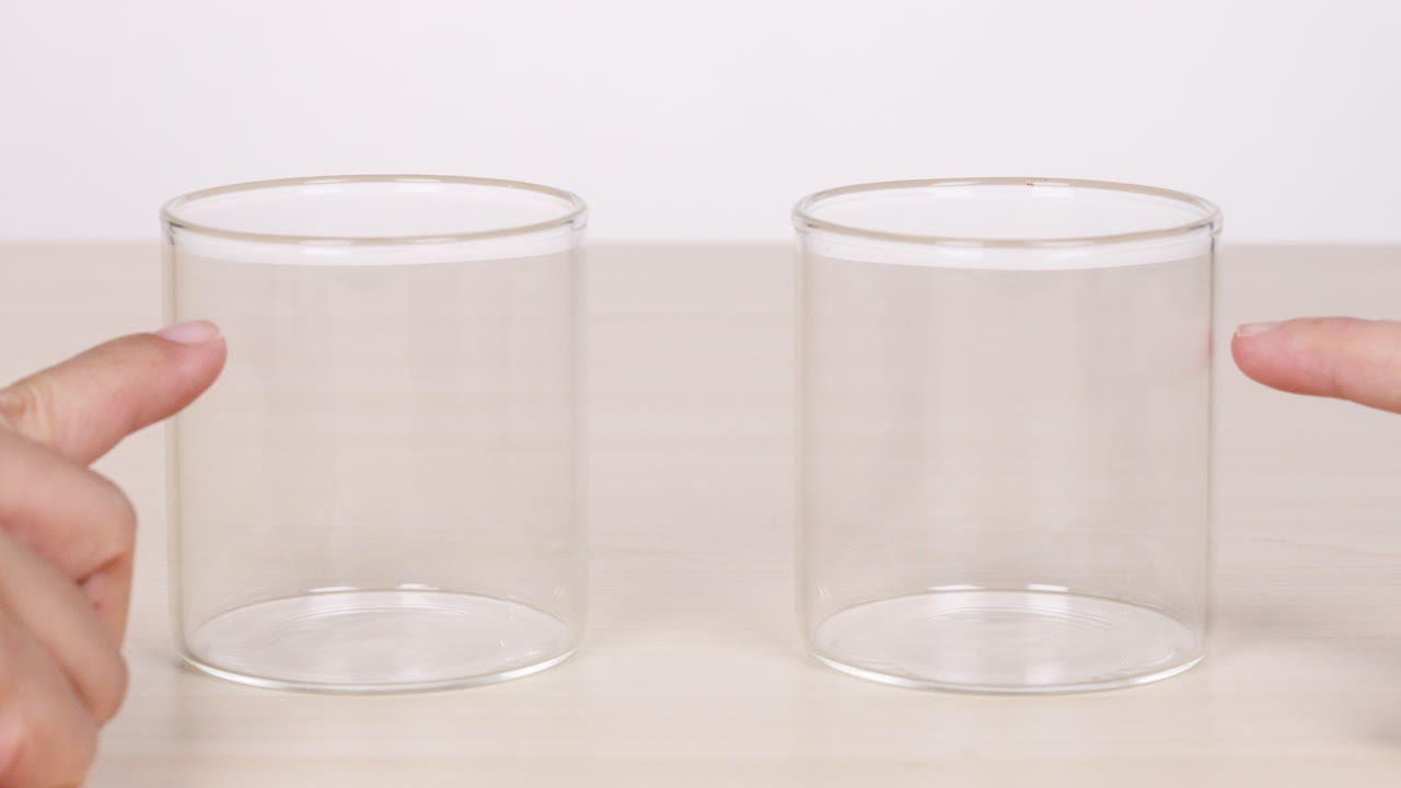 Two fingers point at empty glass containers on a table, then withdraw; neutral lighting