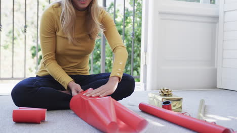 Biracial-woman-sitting-on-floor-packing-christmas-presents,-slow-motion