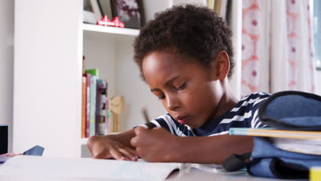 young boy sitting at desk in bedroom and drawing