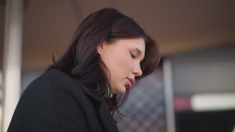 close-up of white lady with pink lips muttering words softly, deeply focused on something in front of her, background features architectural structure with blurred details