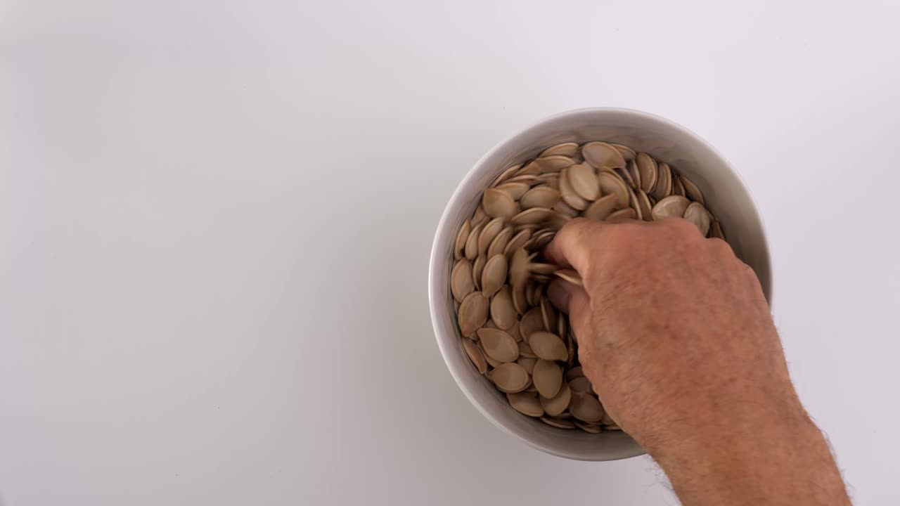 Top view of man cleaning pumpkin seeds in bowl of water after Halloween carving, preparation on white background