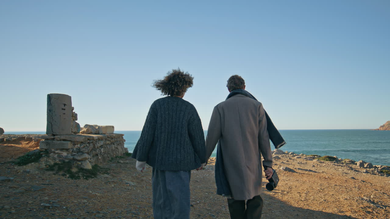 Romantic pair walking ocean beach back view. Diverse couple in love strolling