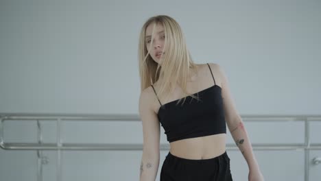 chica en forma con ropa negra actuando contemporáneamente. bailarina muestra movimientos fluidos, cuerpo y manos ondas en la habitación blanca. coreografía de danza de ballet moderno. joven se mueve suavemente