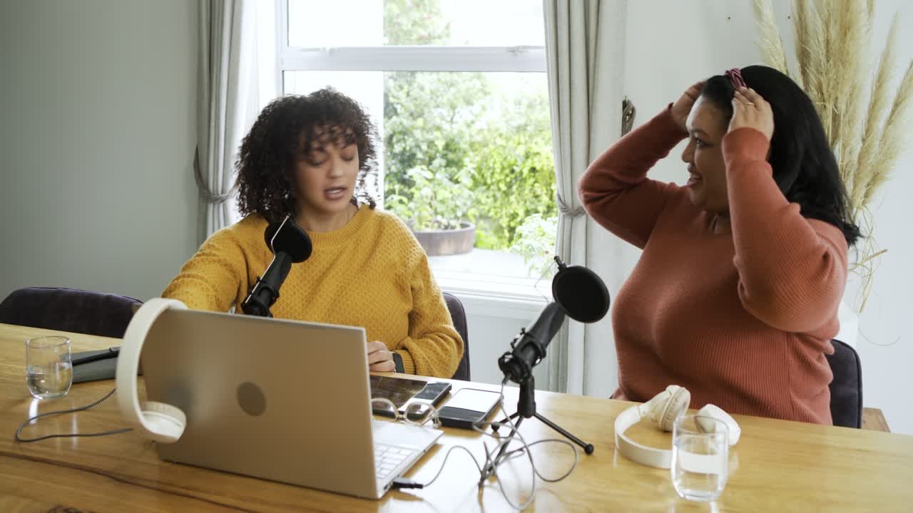 Female podcast cohosts adjusting headphones greeting audience at studio tapping mic ending show