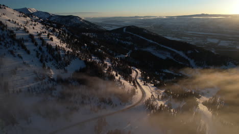 aerial view of winter sunset above snow capped mountain, forest and road