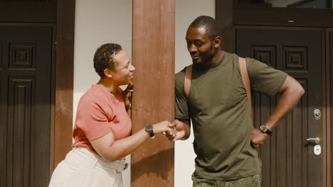 male soldier holding his wife's hand and talking to her while standing together outside home in a sunny day