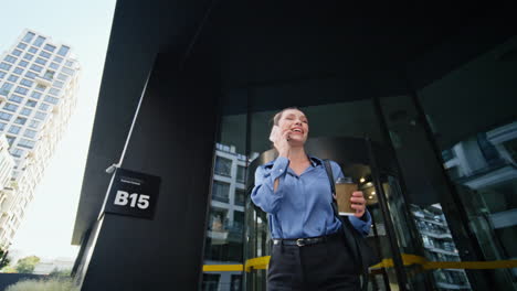 mujer de negocios alegre respondiendo al teléfono móvil saliendo del centro de la oficina. mujer hablando