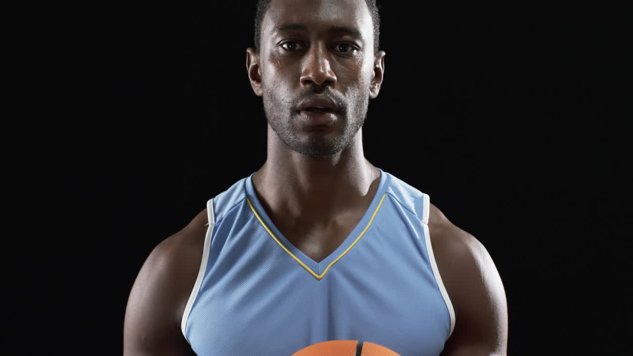 Atleta afroamericano concentrado sosteniendo un balón de baloncesto sobre fondo negro.