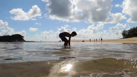 a tan boy casually slides into the frame on a skimboard in shallow water