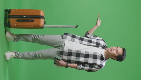 full body of asian male traveler with luggage and passport smiling and pointing to side while standing in the green screen background studio