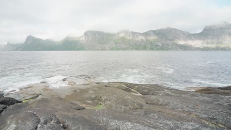 Hiker-Fishing-On-The-Shore-Of-The-Sea-In-Anderdalen-National-Park-In-Senja-Island,-Segla-Norway-With-Mountains-In-The-Background