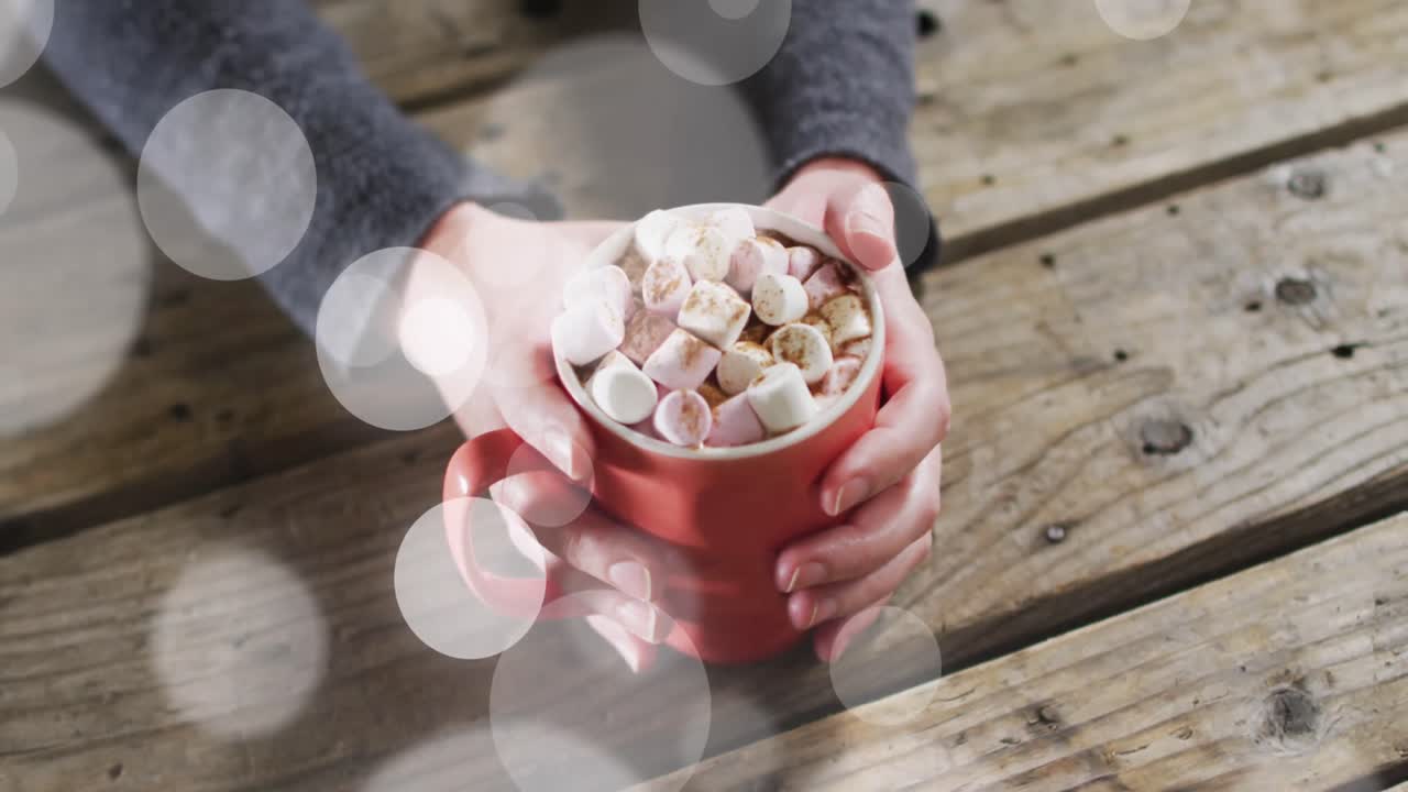 나무 바탕에 뜨거운 초콜릿 마쉬멜로를 가진 할로윈 컵을 들고 있는 여성의 애니메이션.