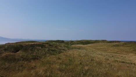 breezy llanddwyn beach island aerial view flying across newborough forest nature reserve grassland towards coastal lighthouse