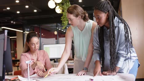 busy diverse female architects discussing blueprints at desk in office, in slow motion