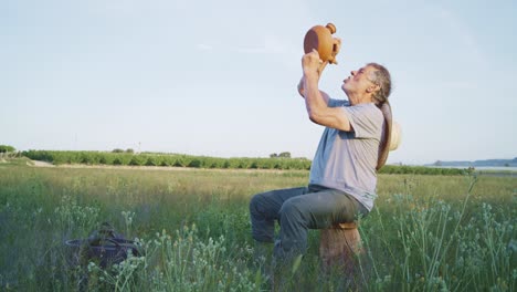 Senior-man-drinking-water-from-clay-teapot-in-field