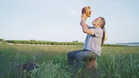 senior man drinking water from clay teapot in field