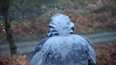 el hombre se sienta con la capucha esperando mientras la nieve cae a su alrededor en una zona rural