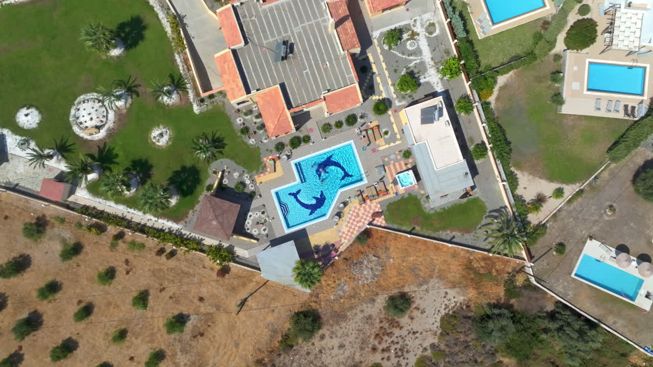 Aerial view rotating above a mom and kids playing ball in a villa pool, sunny day