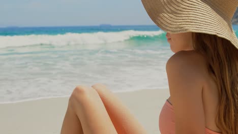 vista lateral de una mujer caucásica con sombrero relajándose en la playa 4k