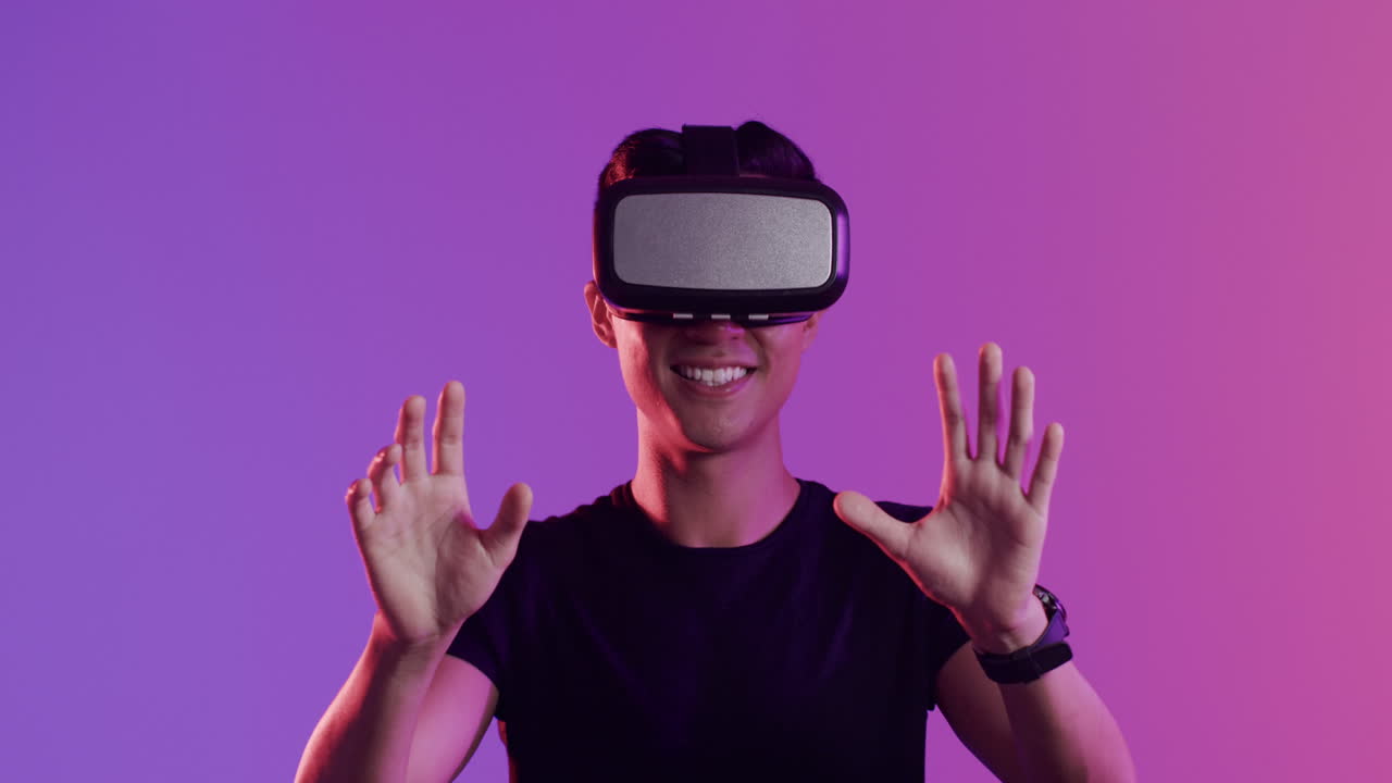 Happy asian man using vr headset and touching virtual screen on purple background, slow motion
