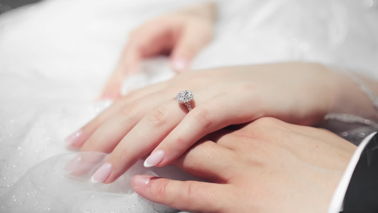 A close up shot of a brides hand wearing a sparkly ring resting on top of the grooms hand