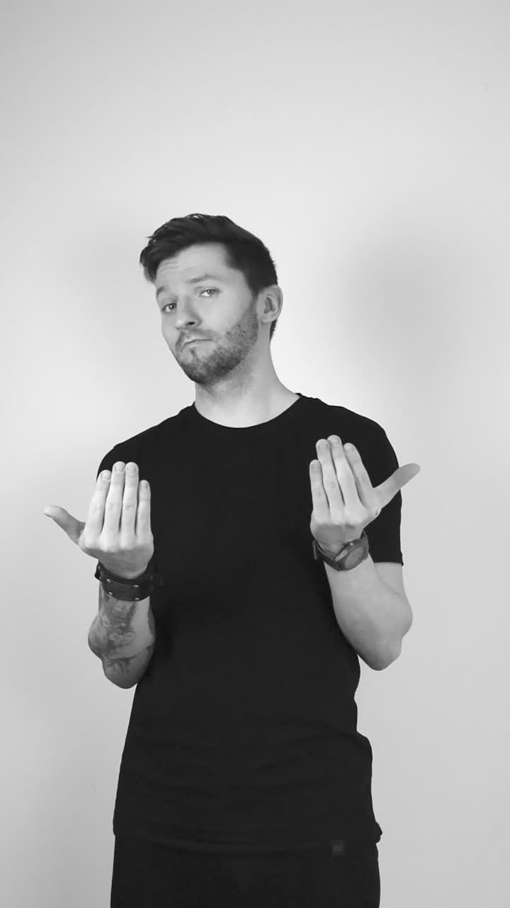 Grayscale footage of a tattooed man with short hair and bear lifting up his arms and making a bring it on or come at me expression with his hands and fingers. Man is confident and is challenging you.