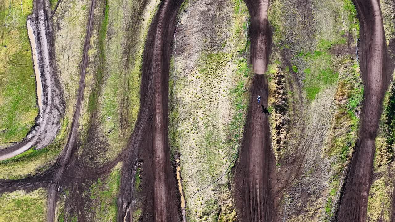 Drone captures dirt bike rider speeding along winding motocross track in bright natural daylight