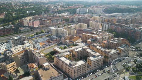 Aerial-drone-backward-moving-shot-over-city-buildings-beside-old-iron-structure,-Gazometro-in-Ostiense-district,-Rome,-Italy-on-a-sunny-day