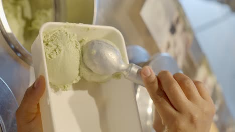 trabajador de heladería sirviendo helado de pistacho en una olla para llevar a casa