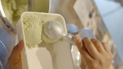 ice cream shop worker serving pistachio ice cream in a pot to take home