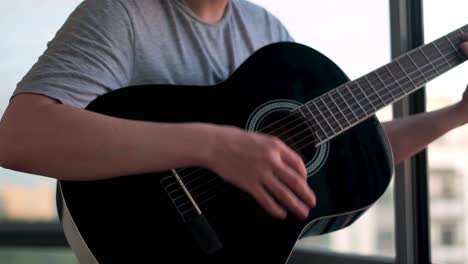 man playing acoustic guitar by the window