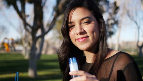 linda mujer hispana soplando burbujas mientras sonríe y se ve feliz y nostálgica al aire libre a la luz del sol de cerca