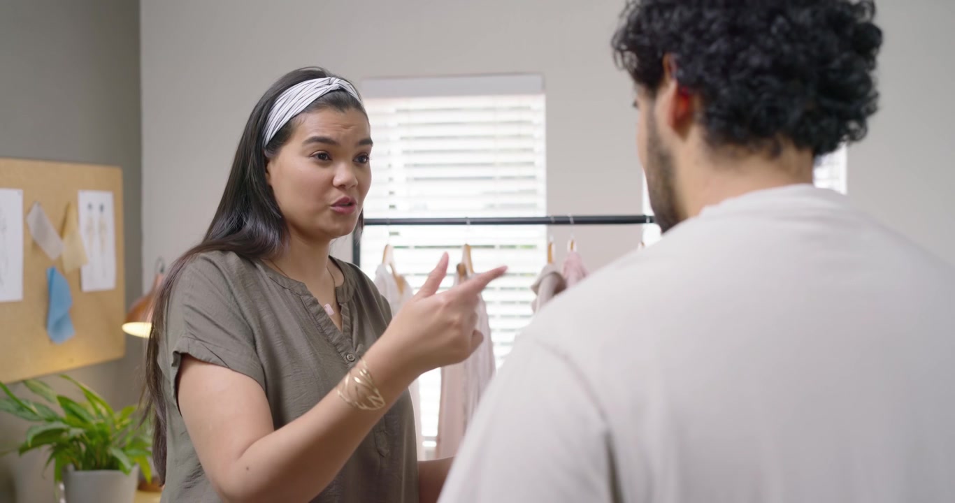 African American team, woman holding swatch starting studio fit talk, pointing rack, man listening
