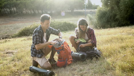 Couple of hikers packing backpacks on grass