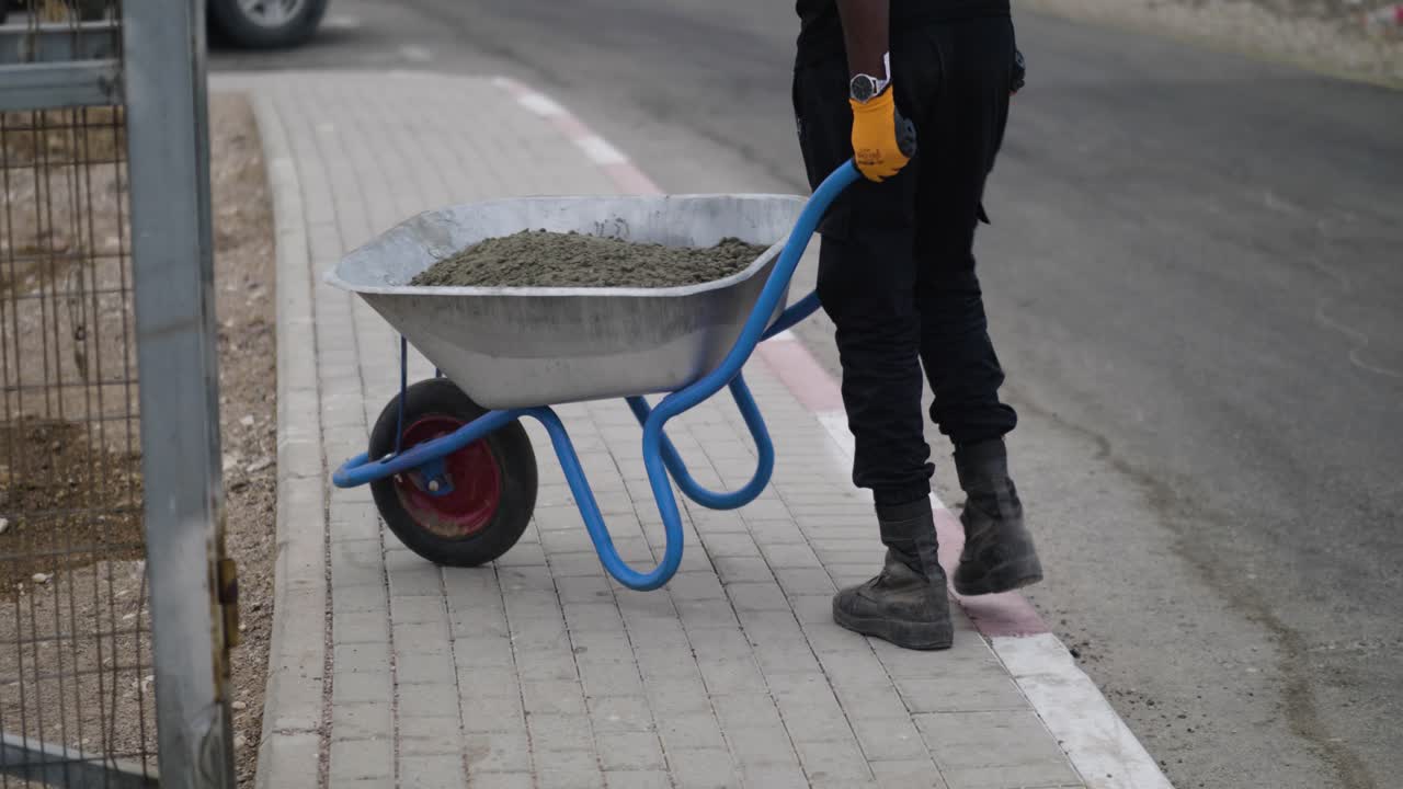 Man grabs handles of a wheelbarrow full of concrete mix and wheels it down the garden