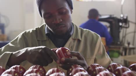 mixed race man focused on cricket ball in factory