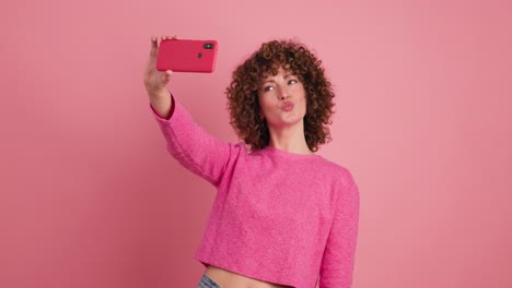 cheerful woman taking self pictures with mobile phone on pink background