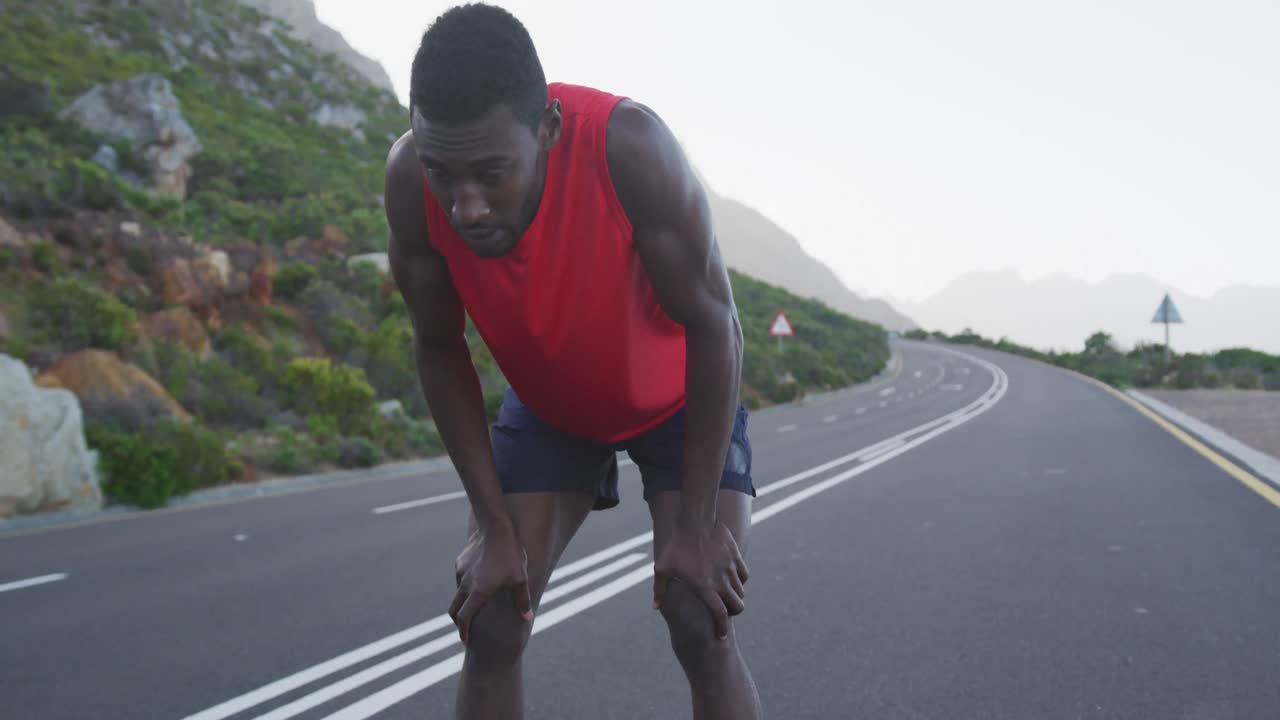 African american man exercising on mountain road stopping to rest during run