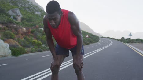 hombre afroamericano haciendo ejercicio en un camino de montaña deteniéndose para descansar durante la carrera
