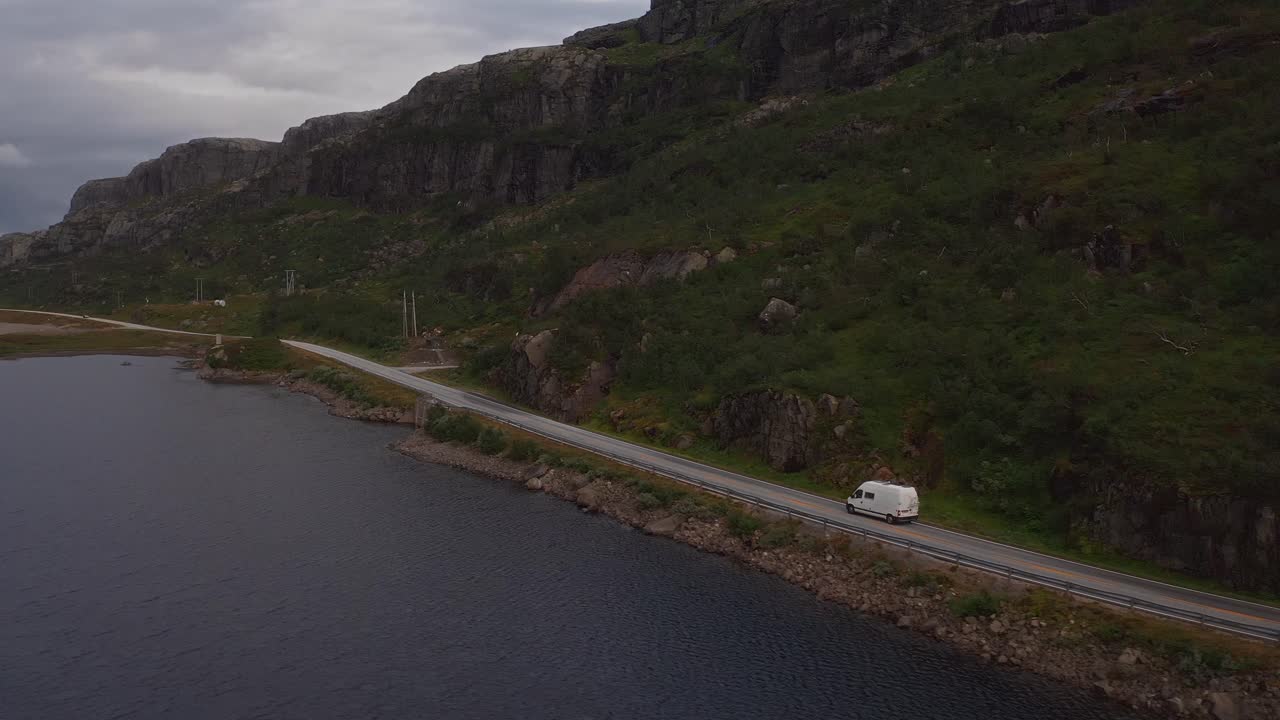 Scenic aerial view of a van driving along a coastal road in Norway, surrounded by mountains