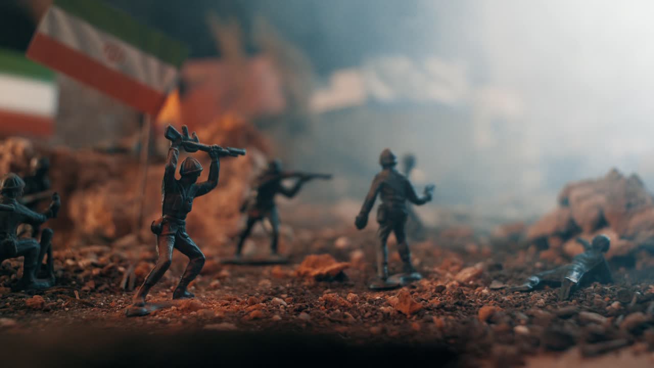 Soldatini di plastica impegnati in un diorama di scena di battaglia. Il campo di battaglia in miniatura è pieno di fumo, terra e bandiere iraniane sullo sfondo.