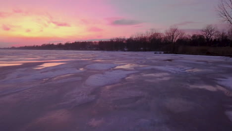 Vibrant-pink-and-orange-sunset-over-a-frozen-coastline-lake-in-southern-Ontario,-Canada