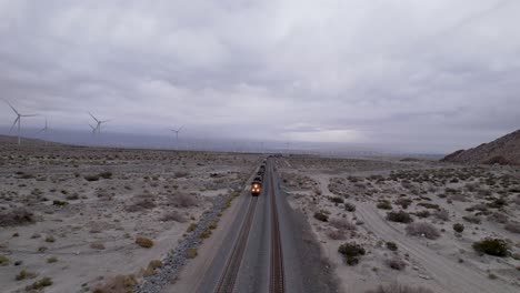 Aerial-Drone-Footage-of-Cargo-Train-in-Palm-Springs-Desert-with-Wind-Farms-in-the-Background,-fast-moving-shot-forward