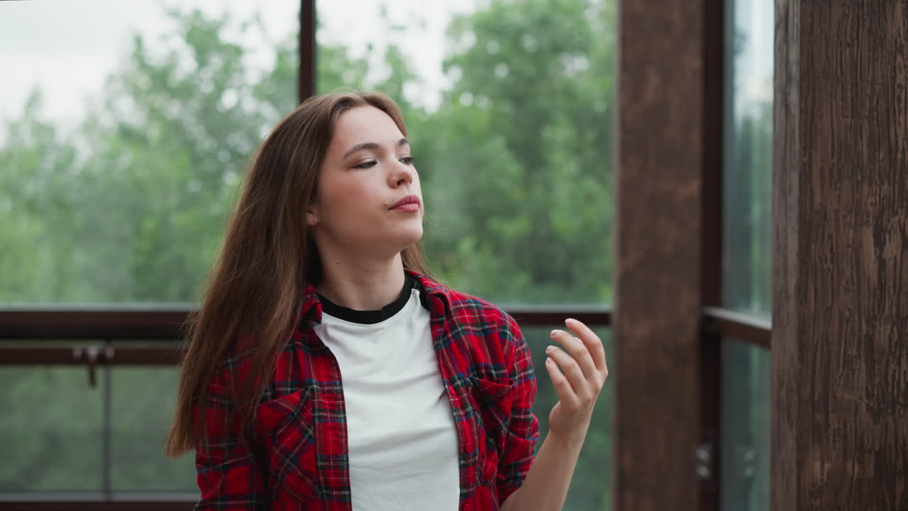 la mujer triste ajusta el peinado contra la ventana. la dama bonita en camisa a cuadros quita el cabello suelto de la cara en la terraza del edificio. estilo de belleza casual
