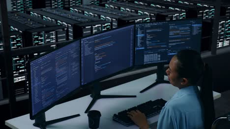vista lateral de una desarrolladora asiática cansada estirándose mientras escribe código con múltiples pantallas de computadora en el centro de datos