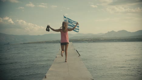 woman shoeless dancing sirtaki on sea pier in front of a greek flag