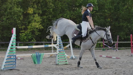 a woman jockey in a black and white suit on a horse makes a jump over the barrier. slow motion: a woman jockey in a black and white suit on a horse makes a jump