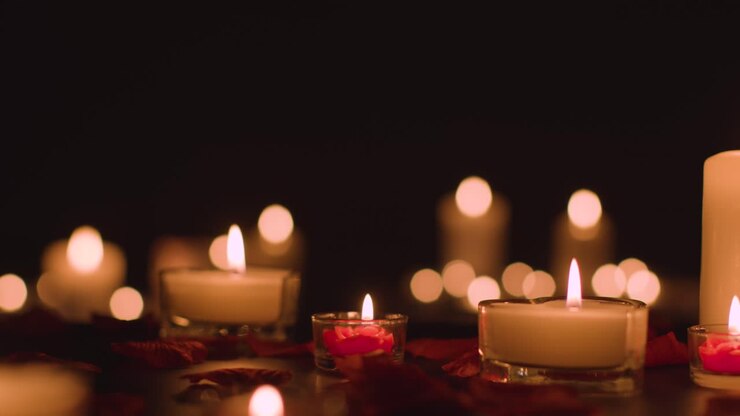 Eye Level Shot Of Romantic Lit Candles On Black Background Covered In Rose Petals With Copy Space