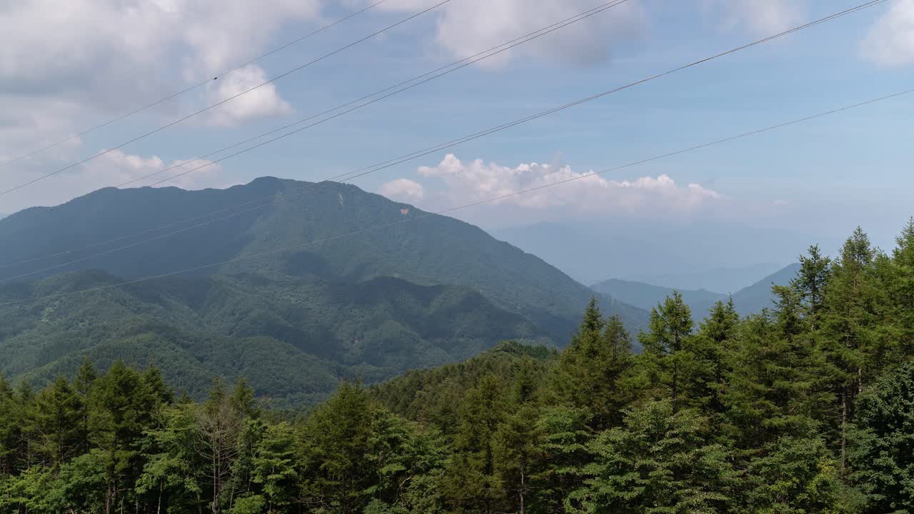 전경에 숲과 녹지가 있는 산에 그림자를 드리우는 구름과 함께 빠르게 움직이는 시간 경과 - 패닝 샷