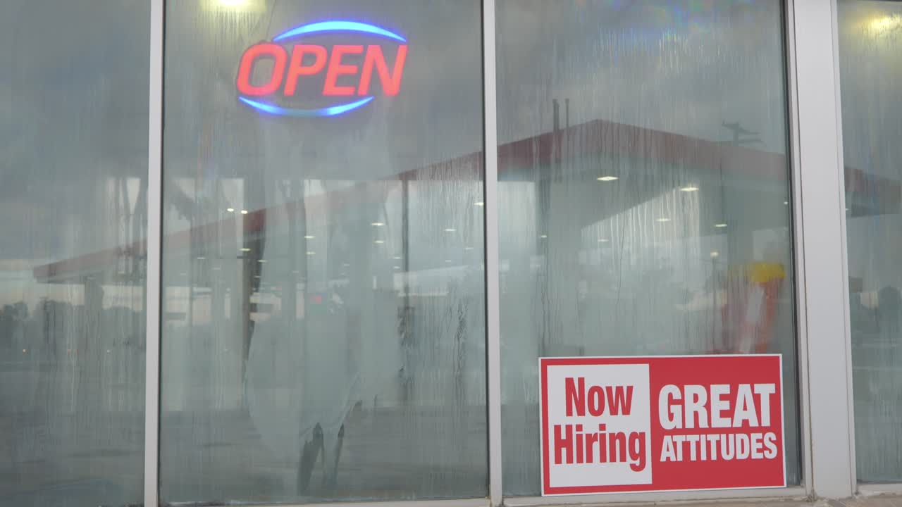 ahora contratando grandes actitudes letrero rojo y blanco brillante en la ventana de lavado de autos con condensación y rocío en vidrio y gasolinera en reflejo, ángulo de cámara estático en cine 4k 30fps ralentizado de 60fps